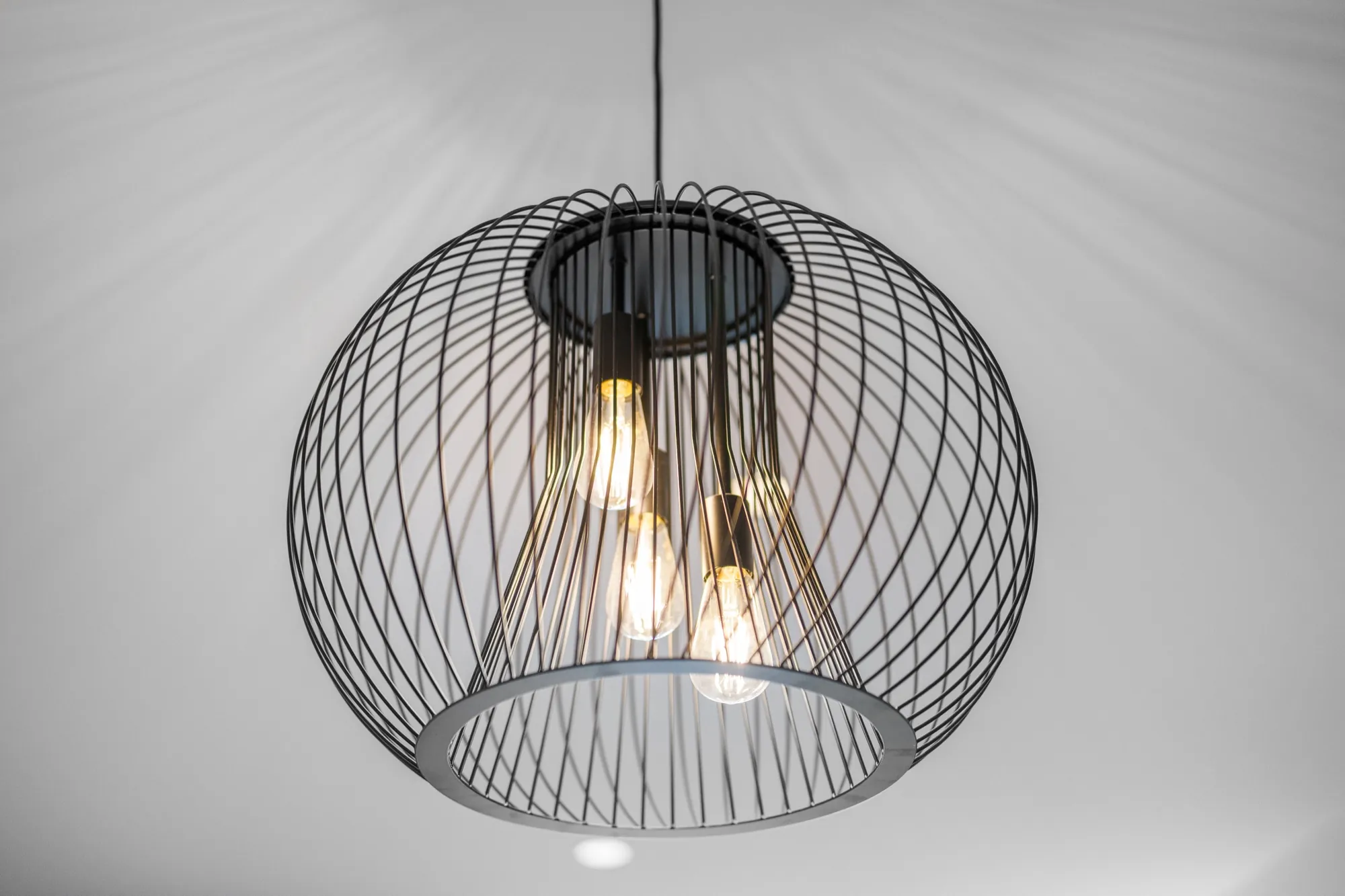 Black wire cage pendant light installed over the dining table in the Bruce apartment