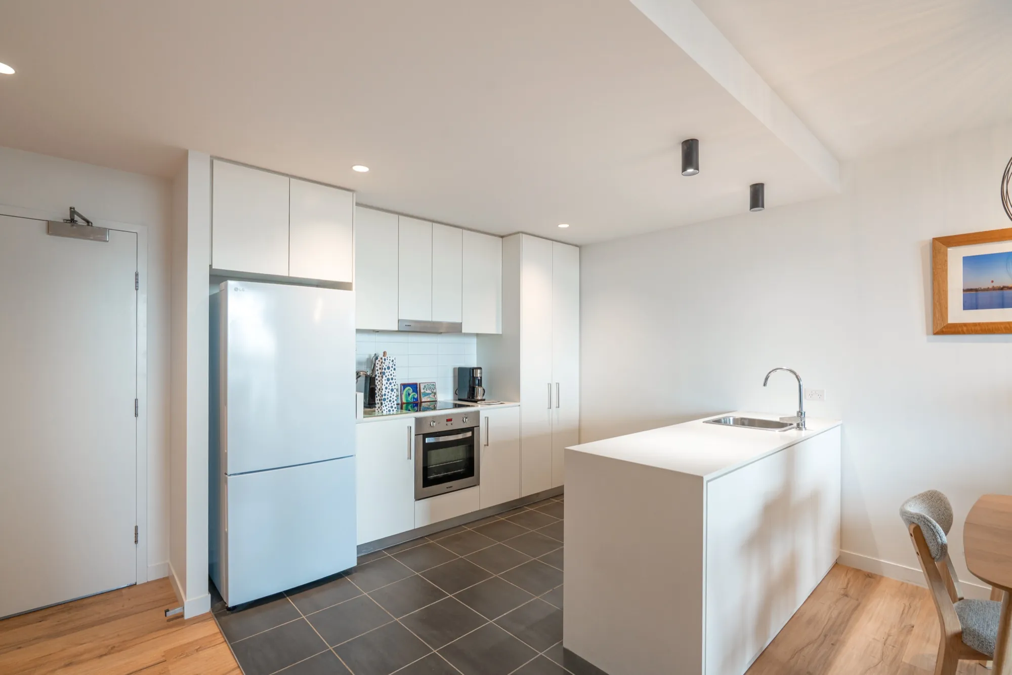Bruce apartment kitchen after the rewire, downlights and clean white finishes throughout