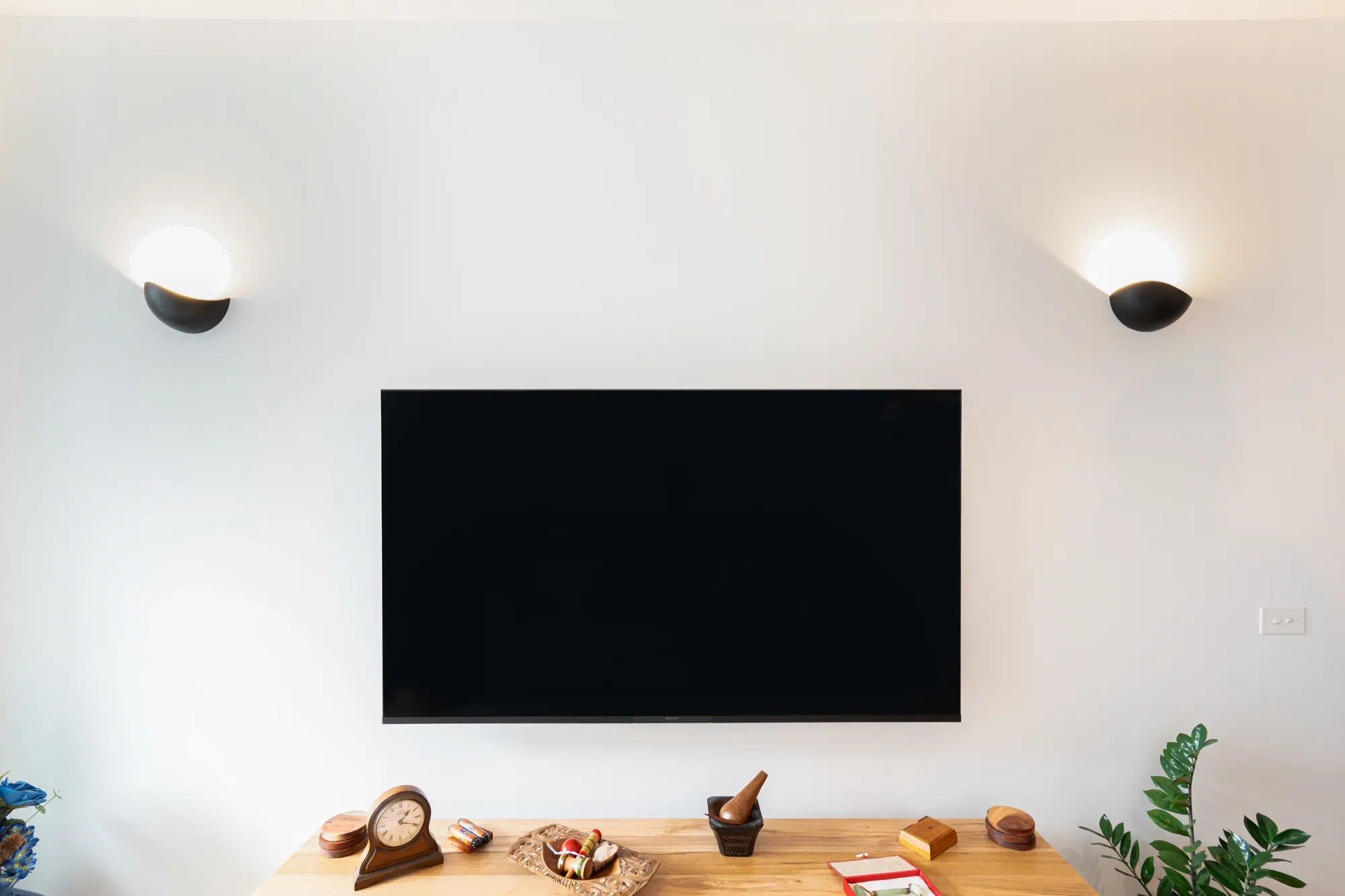 Wall-mounted television flanked by two uplight wall sconces in the Bruce apartment