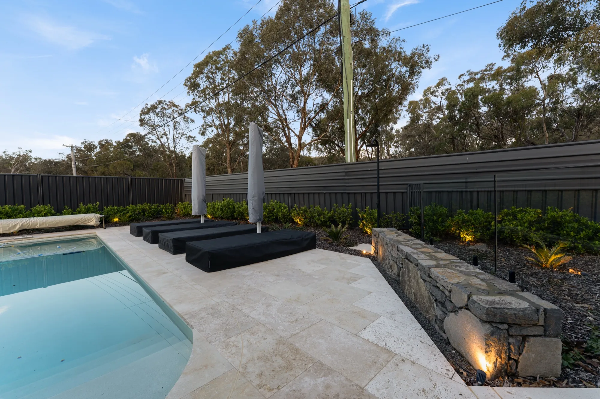 Pool, stone retaining wall and garden lighting at dusk at the Hackett new build
